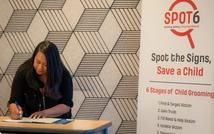 Teresa Agustin, Founder of SPOT6, at desk with Spot the Signs Save a Child banner